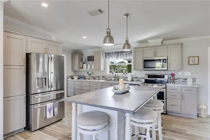 Kitchen with stainless steel appliances, a kitchen breakfast bar, ornamental molding, hanging light fixtures, and a center island