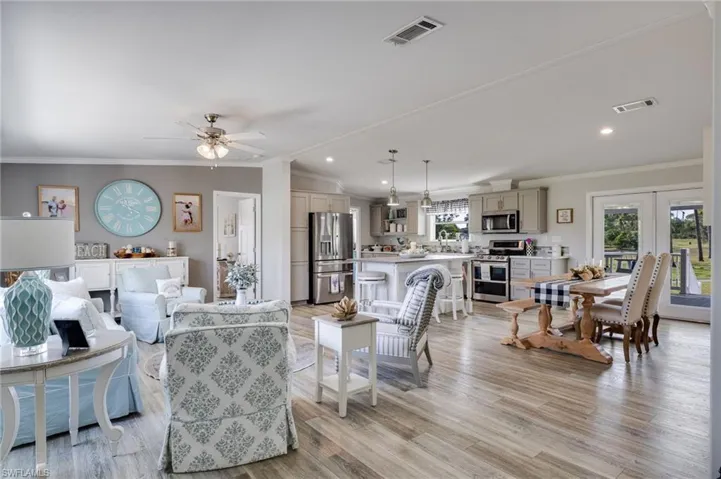 Living room featuring lofted ceiling, ornamental molding, french doors, light wood-type flooring, and a ceiling fan