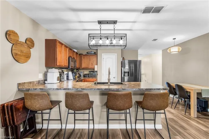 Kitchen with stainless steel appliances, dark countertops, hanging light fixtures, brown cabinetry, and a peninsula