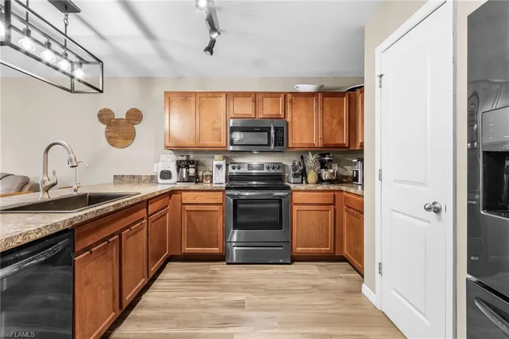 Kitchen with brown cabinets, appliances with stainless steel finishes, light wood-type flooring, and light stone countertops