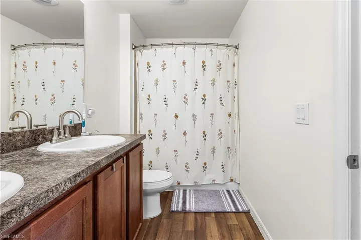 Bathroom with dark wood finished floors, double vanity, and shower / bath combo