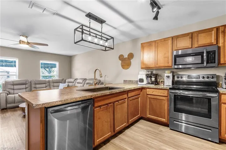 Kitchen with stainless steel appliances, open floor plan, brown cabinetry, light wood-type flooring, and a peninsula