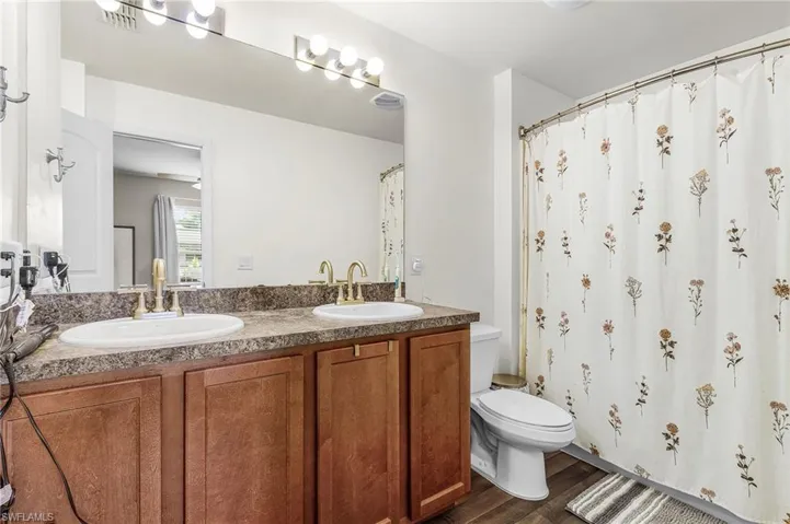 Bathroom featuring dark wood-style flooring, double vanity, and a shower with curtain