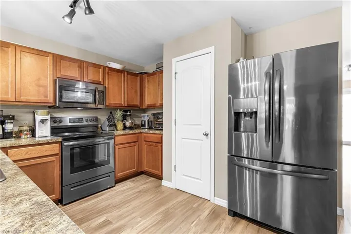 Kitchen with appliances with stainless steel finishes, brown cabinetry, light wood-style flooring, and light stone counters