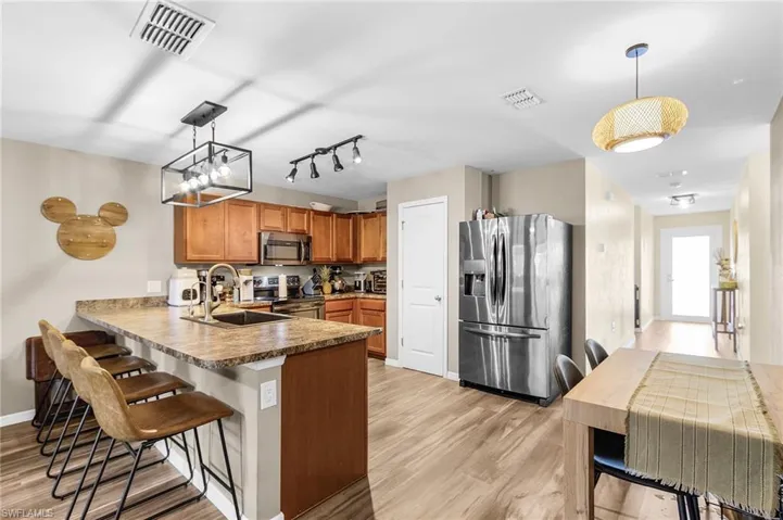 Kitchen featuring decorative light fixtures, brown cabinetry, appliances with stainless steel finishes, a kitchen bar, and light wood-type flooring