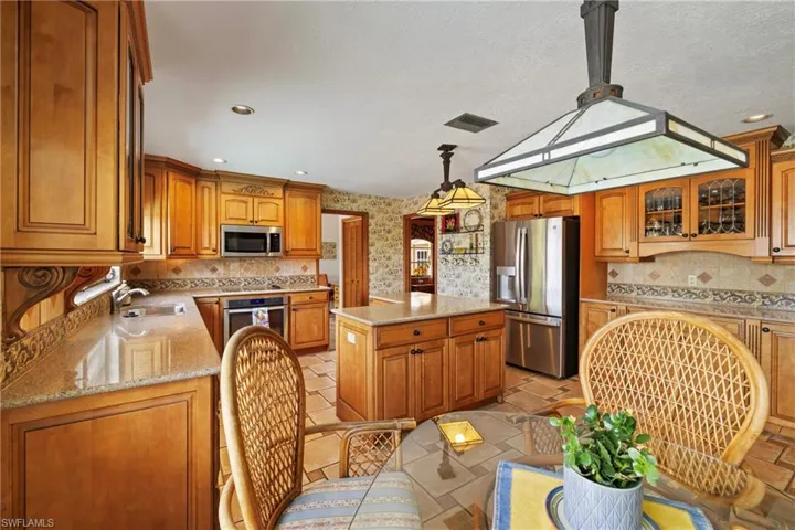 Kitchen with pendant lighting, a kitchen island, sink, light stone countertops, and appliances with stainless steel finishes