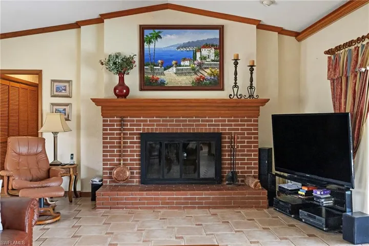 Living room featuring vaulted ceiling, ornamental molding, and a brick fireplace