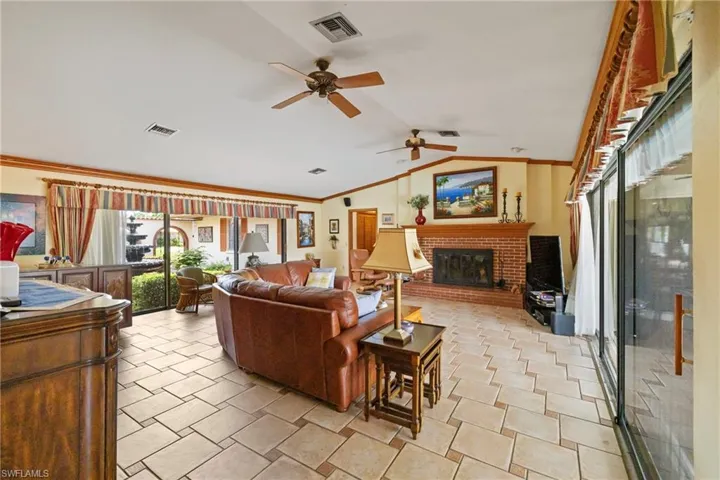 Tiled living room featuring a fireplace, vaulted ceiling, ornamental molding, and ceiling fan