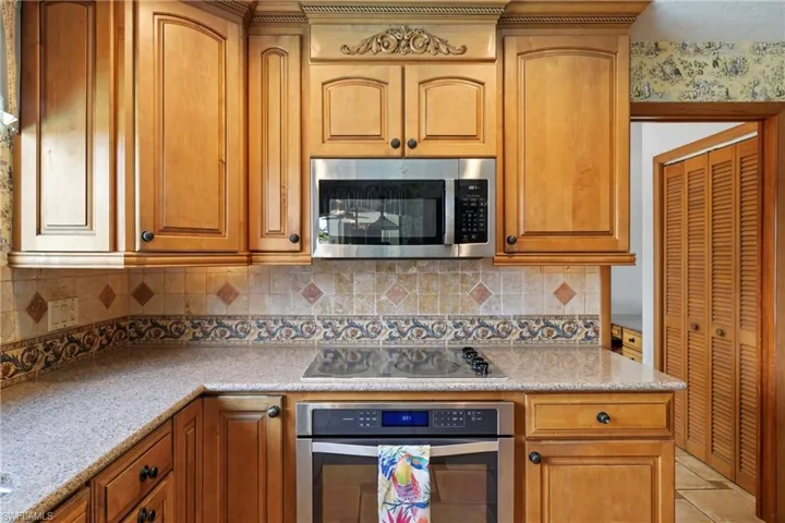 Kitchen featuring stainless steel appliances, light stone counters, light tile patterned floors, and backsplash