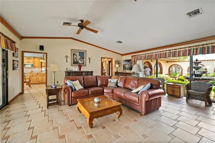 Living room featuring ornamental molding, lofted ceiling, light tile patterned floors, and ceiling fan
