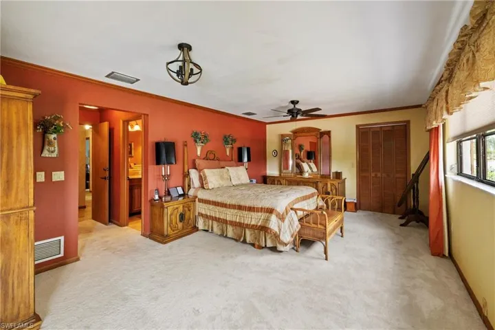 Carpeted bedroom featuring ornamental molding, connected bathroom, ceiling fan, and a closet