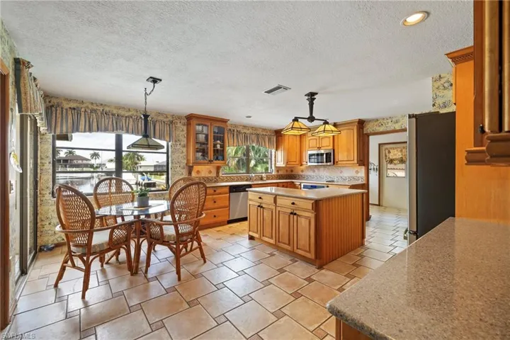 Kitchen with a textured ceiling, decorative light fixtures, a center island, stainless steel appliances, and decorative backsplash