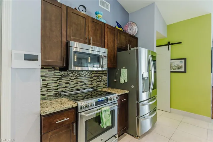 Kitchen featuring stainless steel appliances, a barn door, backsplash, light stone countertops, and light tile patterned floors