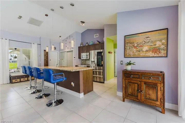 Kitchen with a breakfast bar, appliances with stainless steel finishes, pendant lighting, a kitchen island with sink, and tasteful backsplash