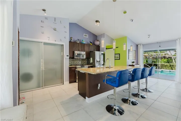Kitchen with dark brown cabinets, a kitchen bar, light stone countertops, backsplash, and hanging light fixtures