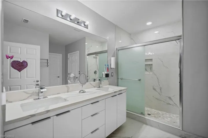 Bathroom featuring vanity with extensive cabinet space, dual sinks, tile floors, and a shower with door