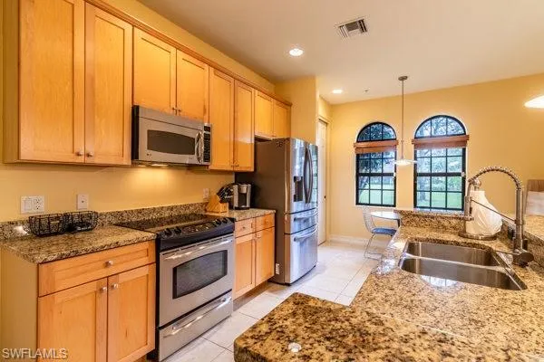 Kitchen featuring stainless steel appliances, sink, light stone countertops, light tile patterned floors, and hanging light fixtures