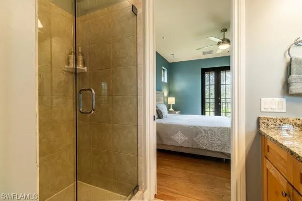 Bathroom with a shower with door, hardwood / wood-style floors, vanity, ceiling fan, and crown molding