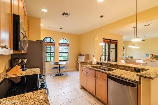 Kitchen with light tile patterned flooring, appliances with stainless steel finishes, decorative light fixtures, light stone countertops, and sink
