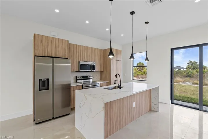 Kitchen featuring stainless steel appliances, light stone counters, hanging light fixtures, modern cabinets, and a kitchen island with sink