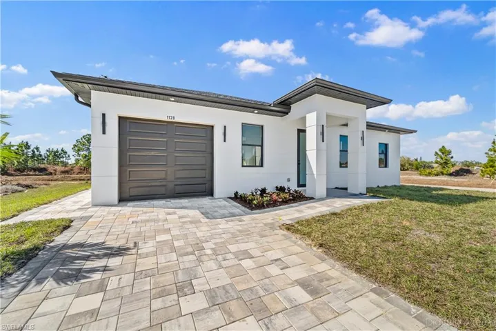 Contemporary house featuring a front lawn, stucco siding, decorative driveway, and a garage
