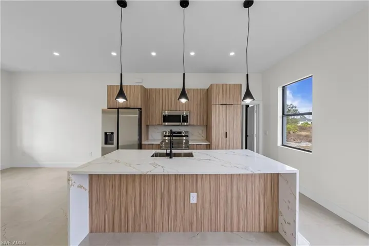 Kitchen featuring light stone countertops, stainless steel appliances, an island with sink, and modern cabinets