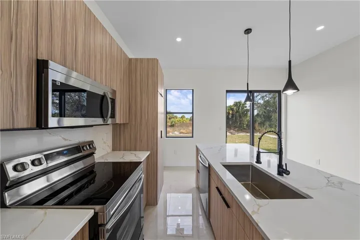 Kitchen featuring wood finish cabinets, stainless steel appliances, modern cabinets, light stone counters, and pendant lighting