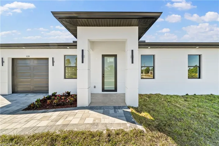 Doorway to property with stucco siding, a lawn, covered porch, and an attached garage