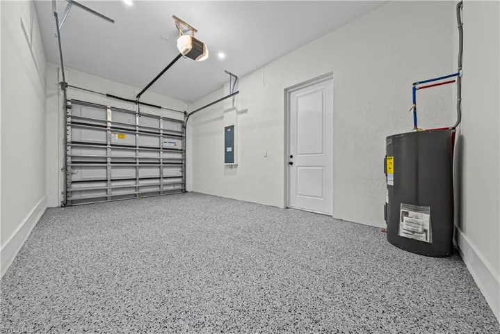 Garage with a garage door opener, water heater, electric panel, and a textured wall