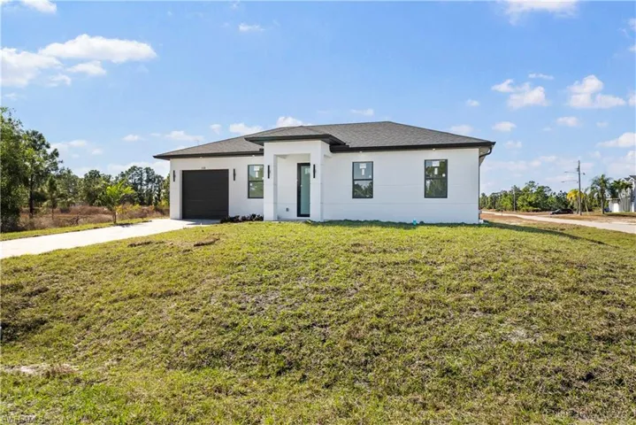 View of front of house featuring a front lawn, driveway, an attached garage, and stucco siding