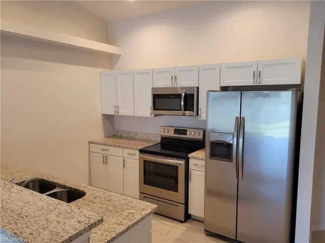Kitchen featuring stainless steel appliances, light stone counters, white cabinetry, and light tile patterned floors