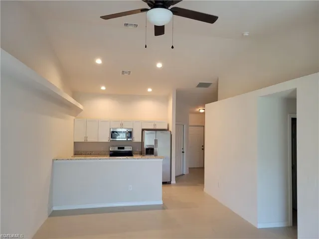 Kitchen with a peninsula, light stone counters, stainless steel appliances, white cabinetry, and ceiling fan