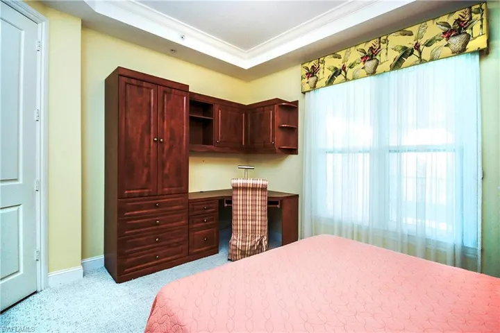 2nd bedroom with light colored carpet, a tray ceiling, built in desk, and multiple windows