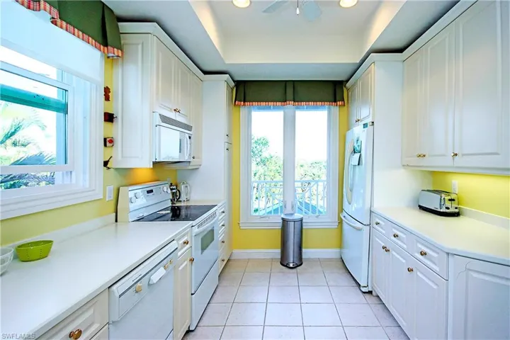 Kitchen featuring white cabinets, tiled patterned floors, ceiling fan, a raised ceiling, and white appliances