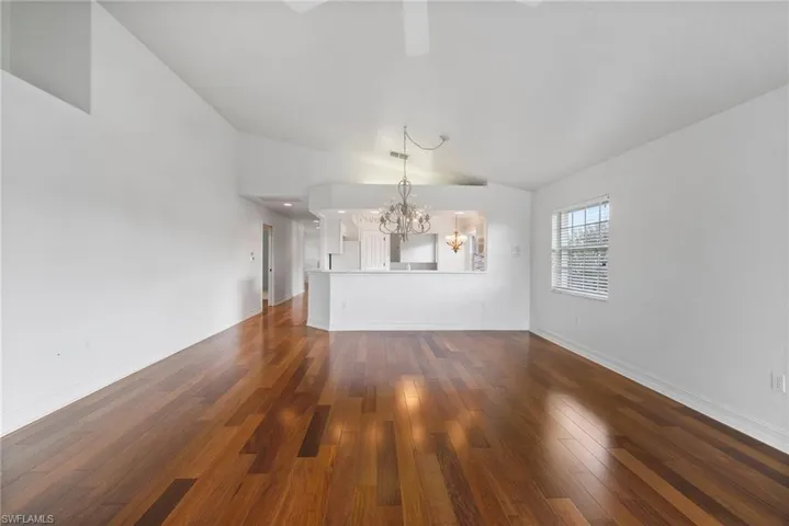 Unfurnished living room with dark wood-type flooring, vaulted ceiling, and a chandelier