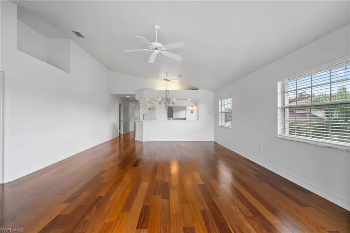 Unfurnished living room with ceiling fan with notable chandelier, vaulted ceiling, and dark hardwood / wood-style floors