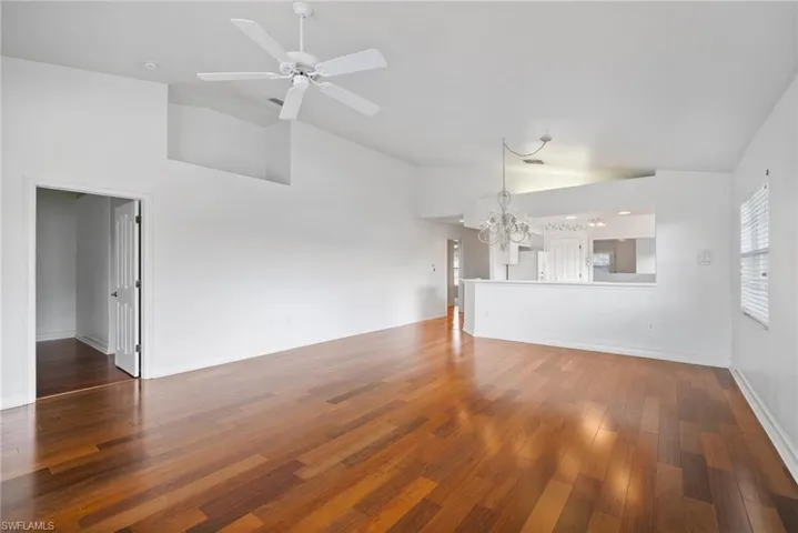 Unfurnished living room with dark hardwood / wood-style floors, high vaulted ceiling, and ceiling fan with notable chandelier