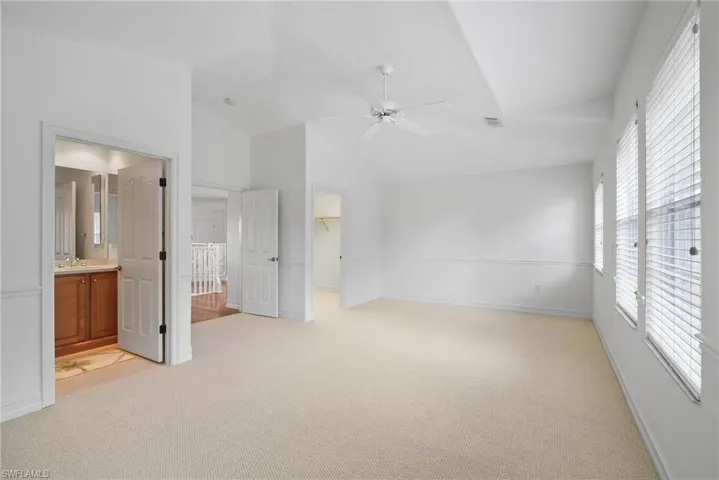 Unfurnished bedroom featuring a closet, light carpet, lofted ceiling, and ensuite bath