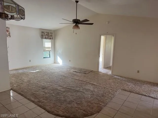 Carpeted spare room featuring vaulted ceiling and ceiling fan