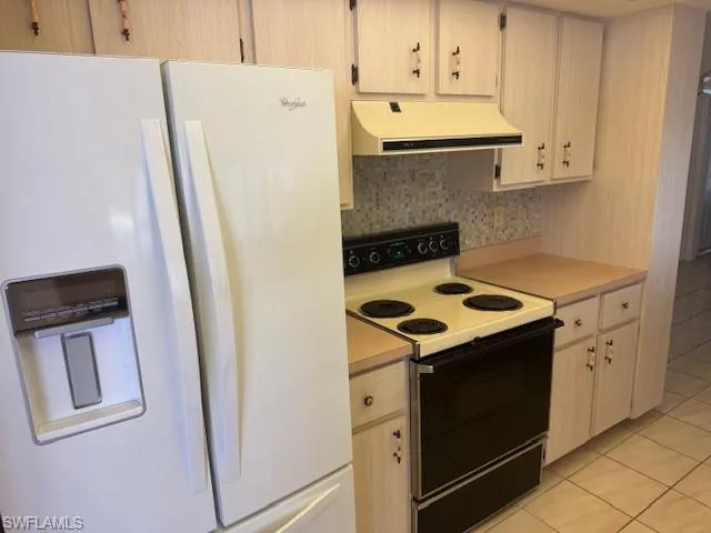 Kitchen featuring backsplash, light brown cabinets, light tile patterned floors, and white appliances