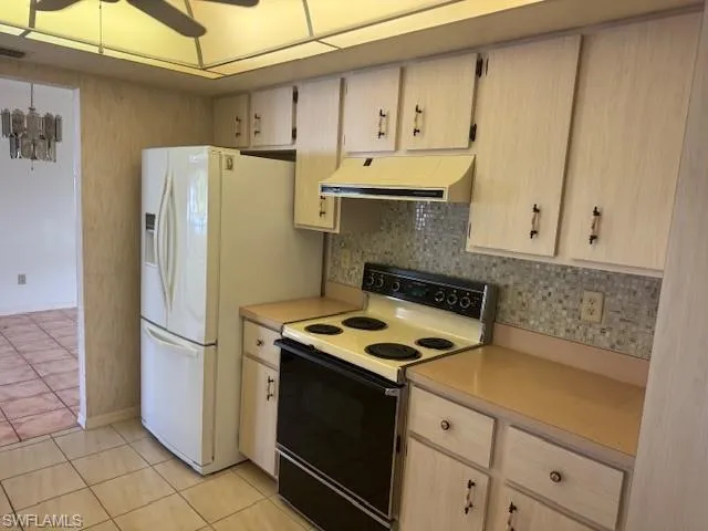 Kitchen featuring decorative backsplash, light brown cabinets, white appliances, and light tile patterned floors