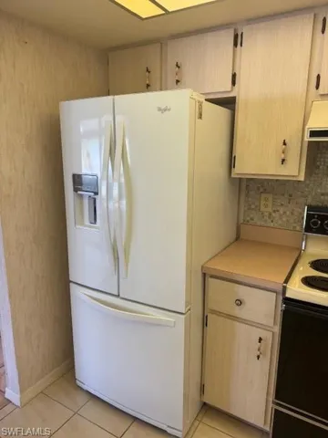 Kitchen featuring stove, light brown cabinetry, range hood, white fridge with ice dispenser, and light tile patterned flooring