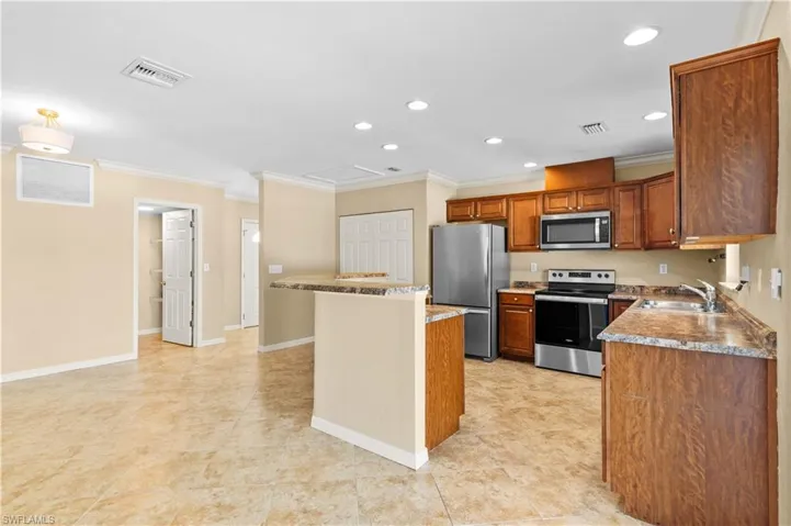 Kitchen with a kitchen island, stainless steel appliances, ornamental molding, sink, and light stone countertops