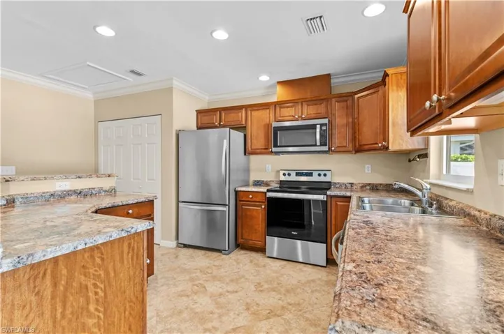 Kitchen with crown molding, stainless steel appliances, light stone countertops, and sink
