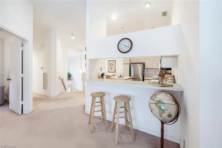 Kitchen featuring a breakfast bar, light countertops, freestanding refrigerator, light carpet, and a peninsula