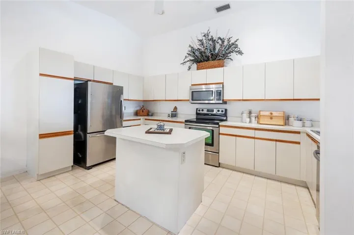 Kitchen with light countertops, stainless steel appliances, a kitchen island, white cabinets, and high vaulted ceiling