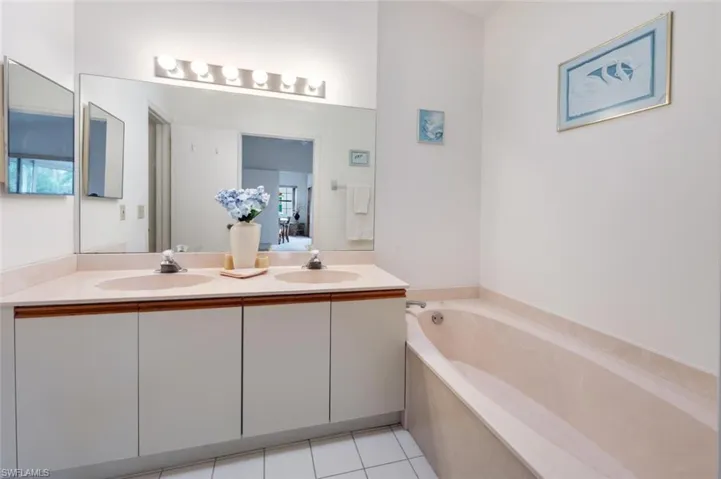 Bathroom featuring light tile patterned flooring, double vanity, and a garden tub