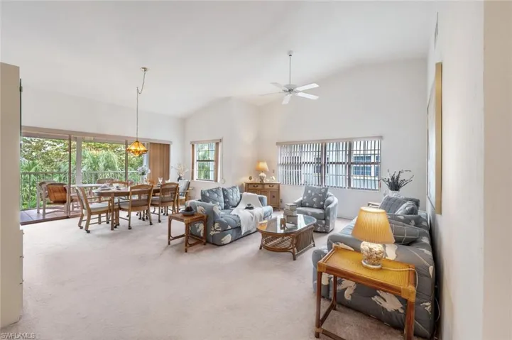 Carpeted living room with healthy amount of natural light, high vaulted ceiling, and a ceiling fan