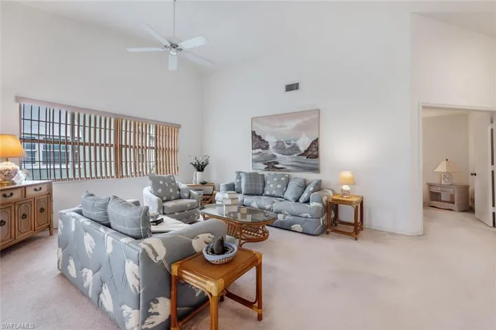 Living area featuring high vaulted ceiling, light carpet, and a ceiling fan