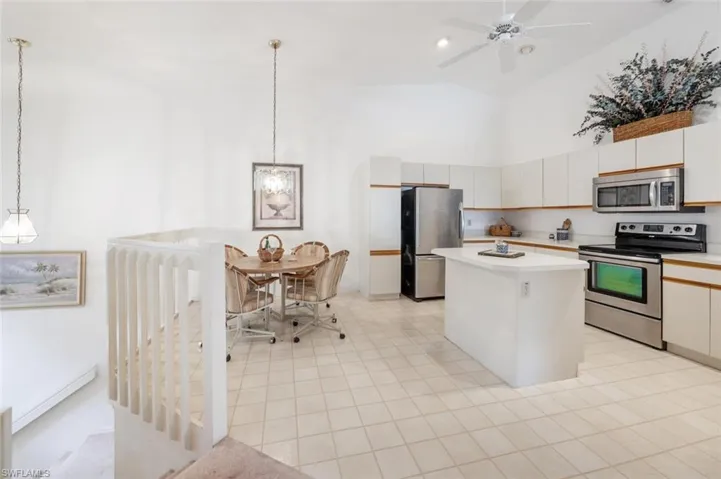 Kitchen featuring light countertops, stainless steel appliances, decorative light fixtures, a kitchen island, and high vaulted ceiling